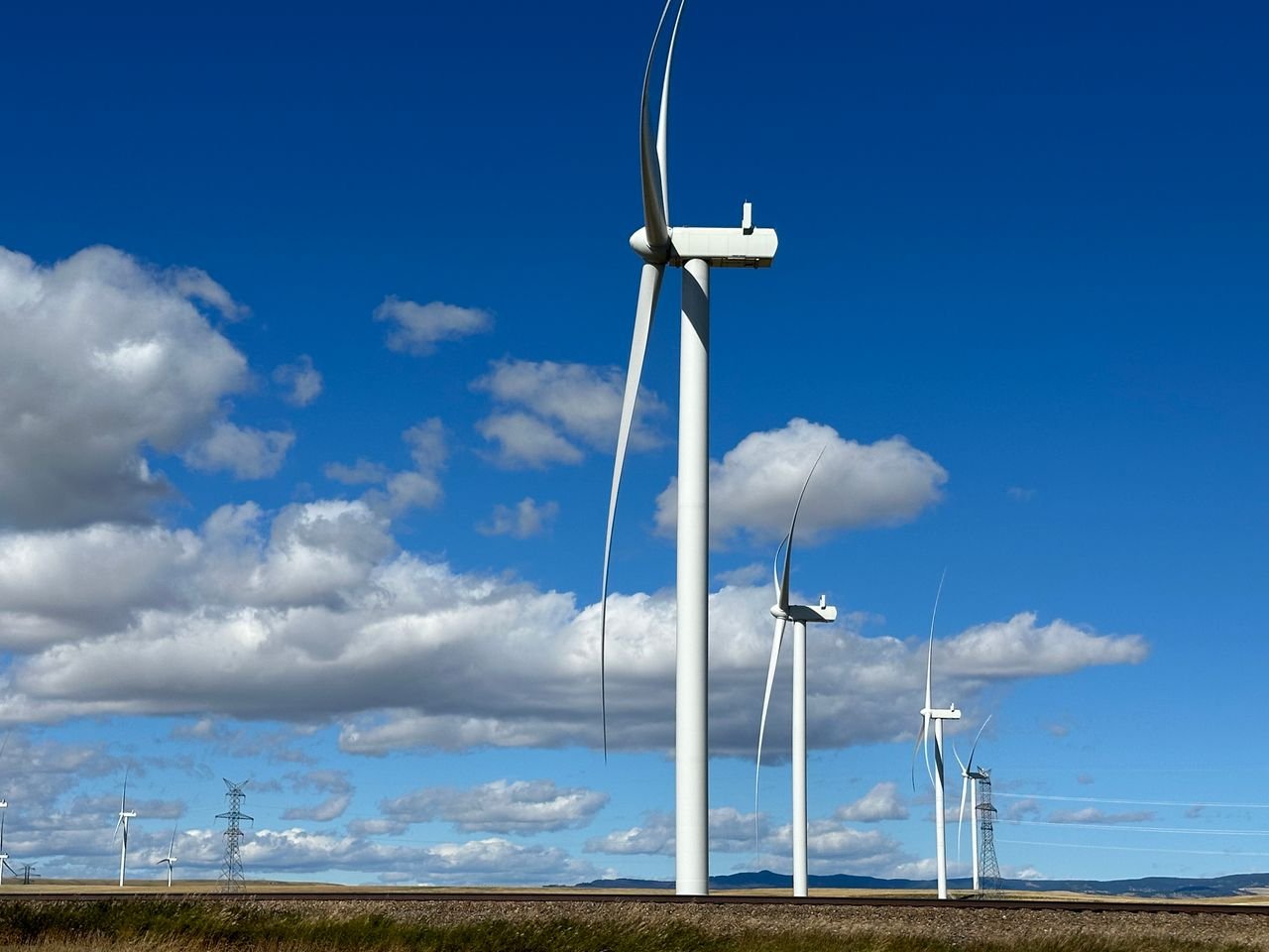 ours-journey Wind turbines in open landscape with blue sky and clouds, emphasizing renewable energy.