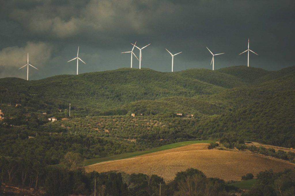 A picturesque view of wind turbines on green hills under dramatic clouds, showcasing sustainable energy.